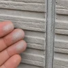 ひび割れた縦目地のある灰色の外壁に触れ、白い粉が付着した指先