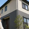 青空の下、白と濃いグレーの外壁を持つ二階建て住宅を手前の女性が見上げている