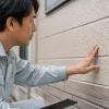 作業着を着た男性が建物の外壁に手を当て、表面の状態を確認している
