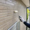 ヘルメットと手袋を着けた作業員が、足場の上でローラーを使い外壁を塗っている