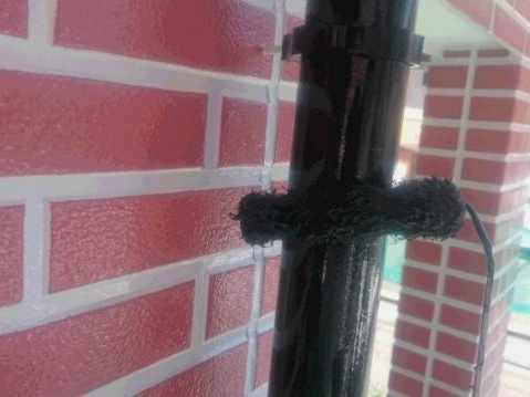 M様邸の縦樋を濃い色で塗装している工程